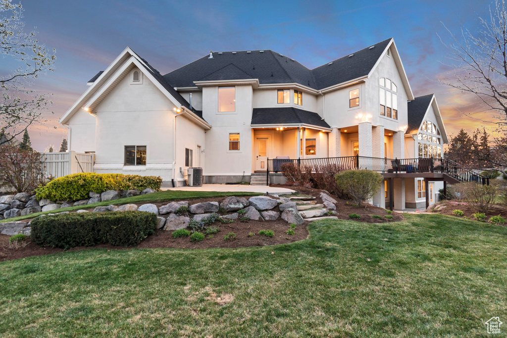 Back of property at dusk featuring central AC unit, a yard, and stucco siding