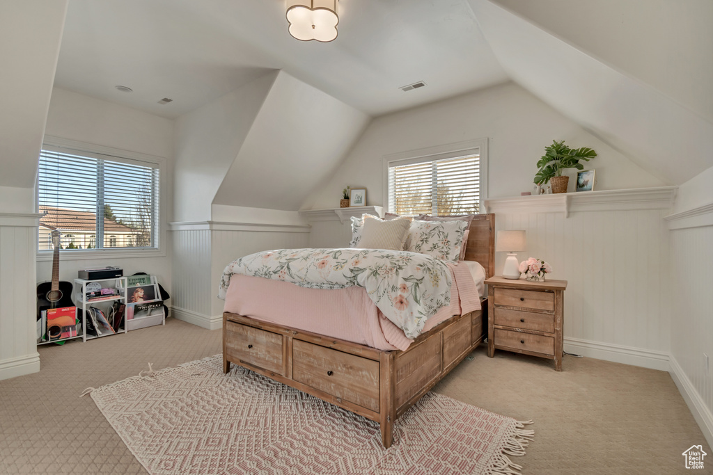 Carpeted bedroom with a decorative wall, visible vents, wainscoting, and vaulted ceiling
