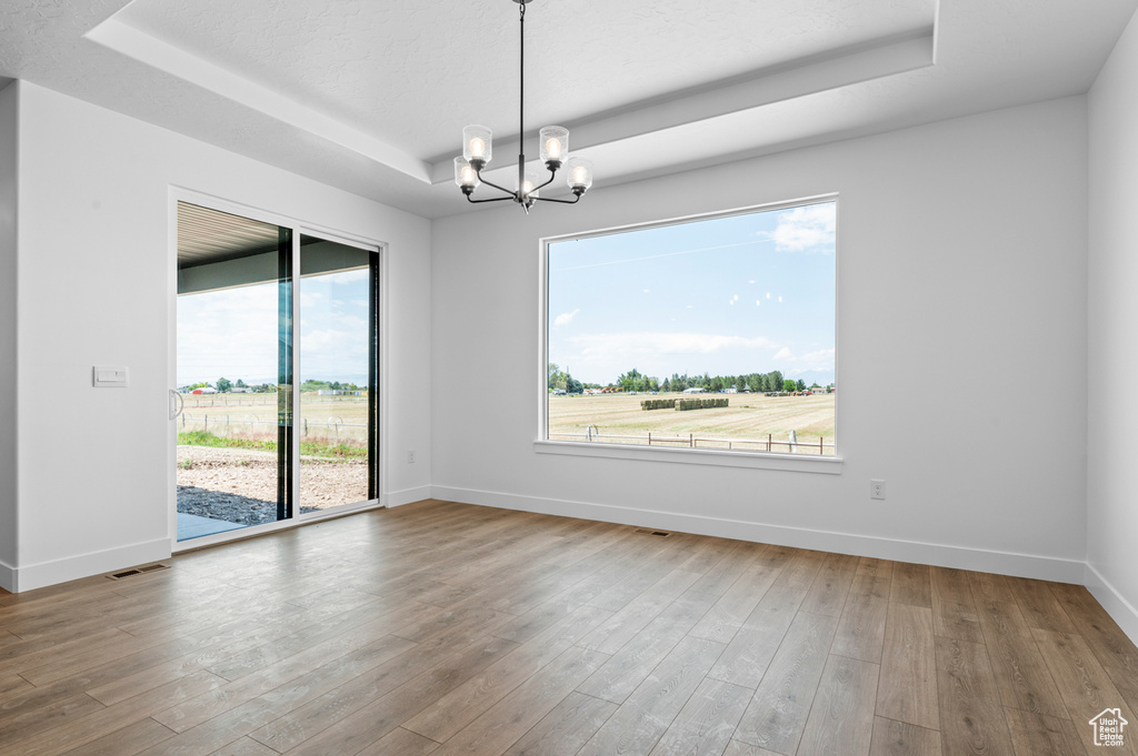 Unfurnished room featuring a tray ceiling, a chandelier, and hardwood / wood-style floors