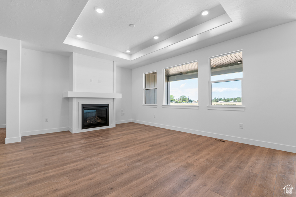Unfurnished living room featuring a raised ceiling, wood finished floors, a glass covered fireplace, and recessed lighting