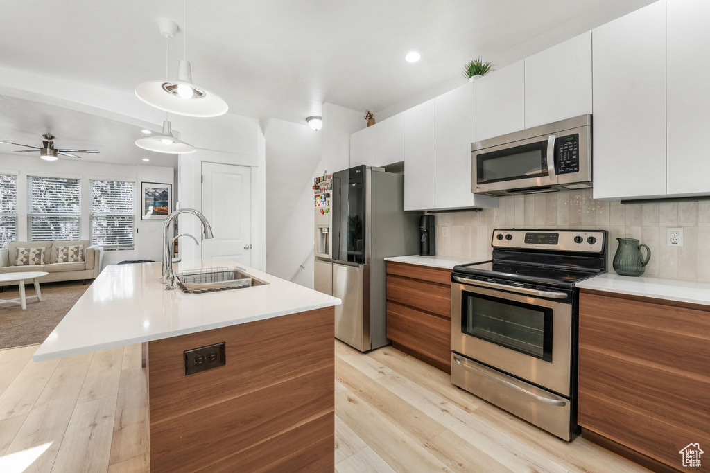 Kitchen with light wood-style flooring, white cabinets, a sink, light countertops, and stainless steel appliances