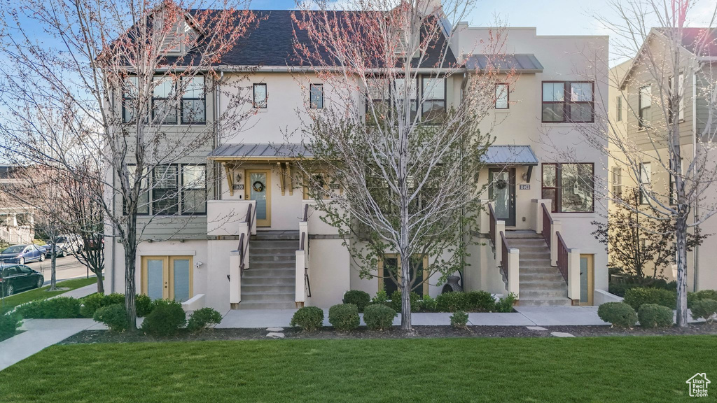 Townhome / multi-family property with a front lawn, stairs, and stucco siding
