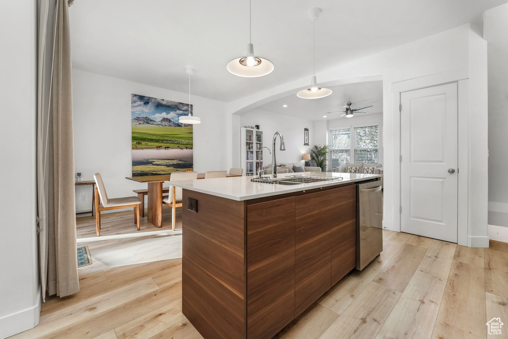 Kitchen featuring a center island with sink, modern cabinets, stainless steel dishwasher, arched walkways, and light wood finished floors