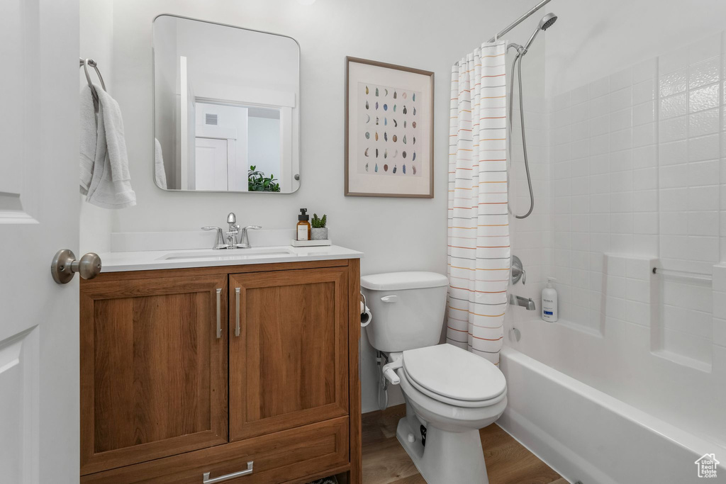 Bathroom featuring toilet, wood finished floors, vanity, and shower / bathtub combination with curtain