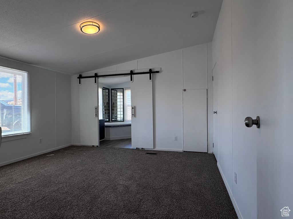 Empty room featuring vaulted ceiling, carpet floors, a barn door, baseboards, and a smoke detector