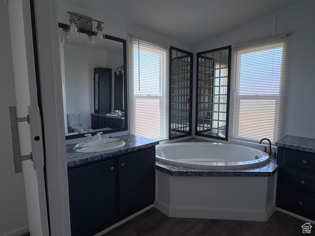 Full bath featuring healthy amount of natural light, a bath, vanity, lofted ceiling, and wood finished floors