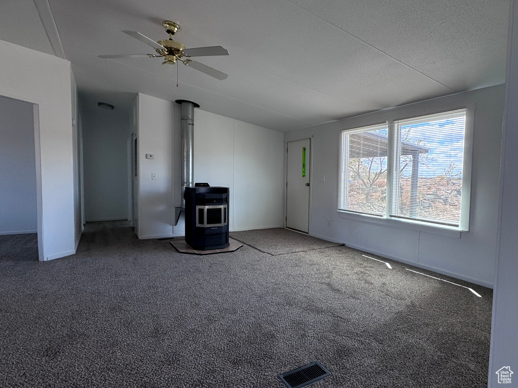 Unfurnished living room with a wood stove, a ceiling fan, carpet, vaulted ceiling, and baseboards