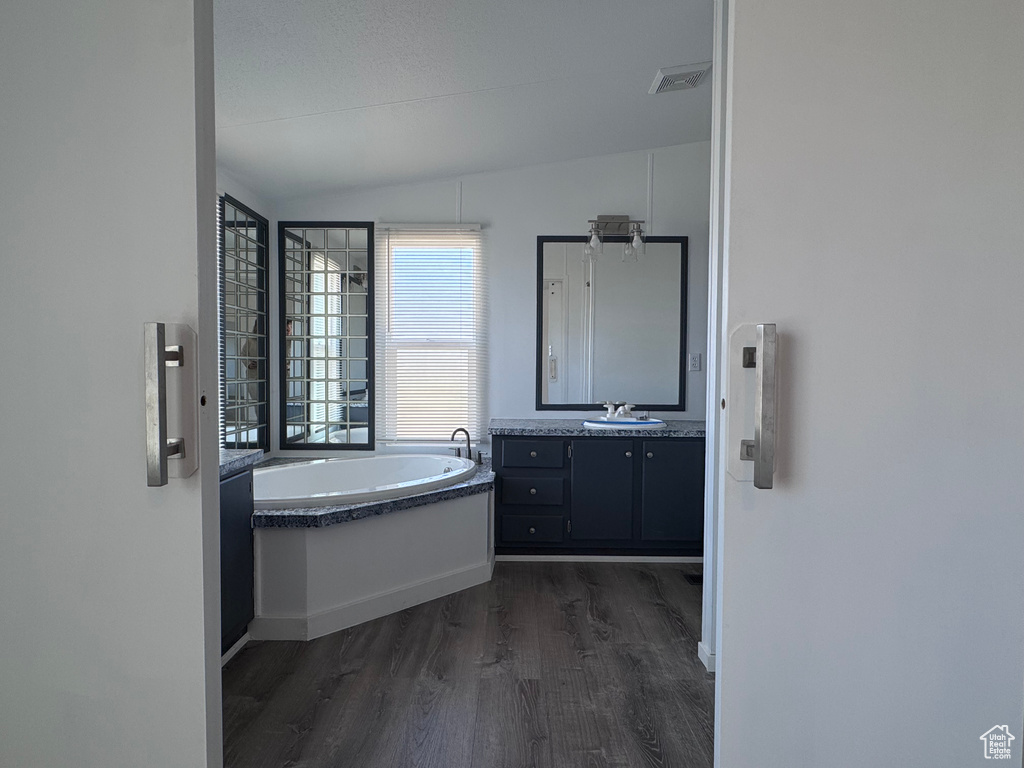 Full bath featuring lofted ceiling, wood finished floors, a bath, vanity, and baseboards