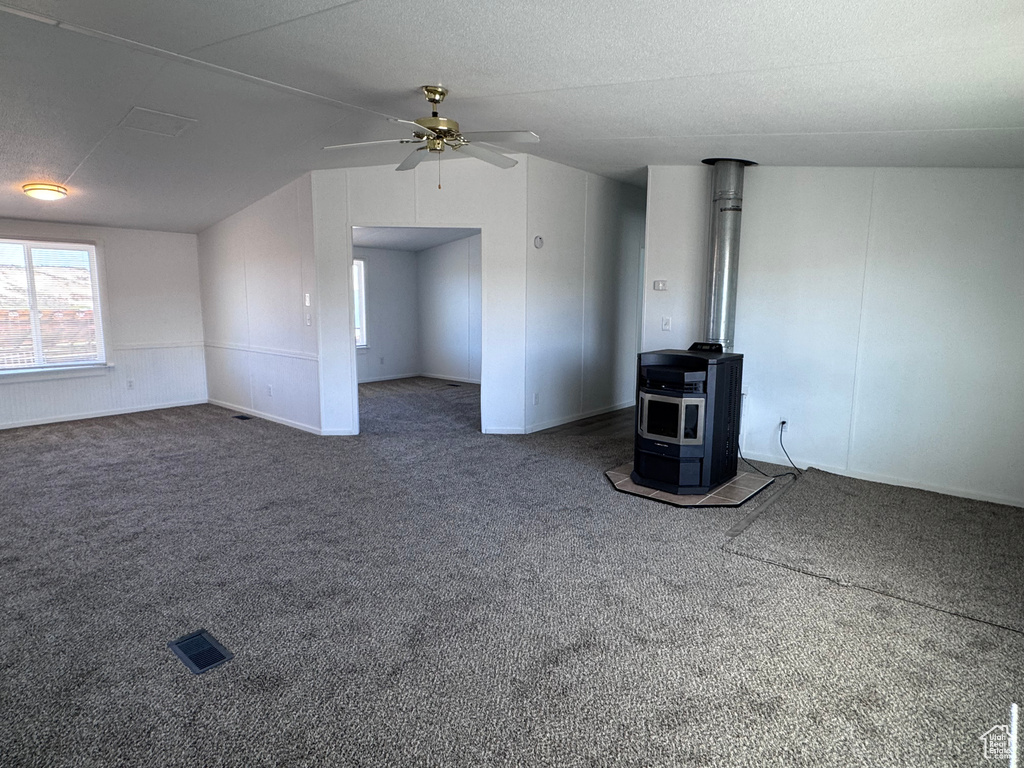 Carpeted spare room with a wood stove, a ceiling fan, and lofted ceiling