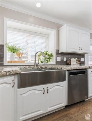 Kitchen featuring stainless steel dishwasher, ornamental molding, white cabinets, tasteful backsplash, and a sink