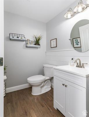 Half bath with toilet, wood finished floors, and vanity