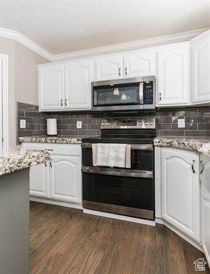 Kitchen with dark wood-style flooring, crown molding, appliances with stainless steel finishes, light stone countertops, and white cabinetry