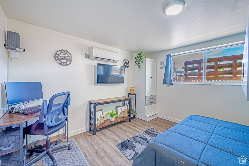Bedroom with baseboards, a wall unit AC, and wood finished floors