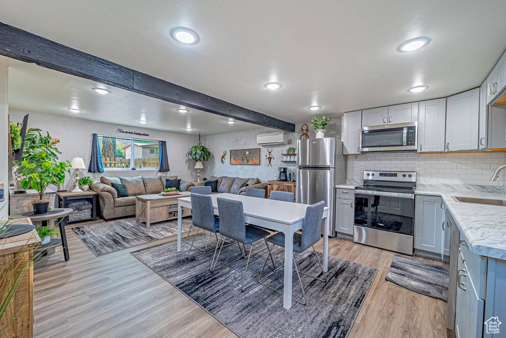 Kitchen with an AC wall unit, light wood-style flooring, decorative backsplash, stainless steel appliances, and a sink
