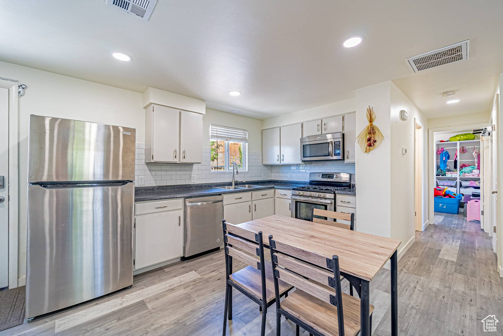 Kitchen with dark countertops, visible vents, light wood-style flooring, and appliances with stainless steel finishes