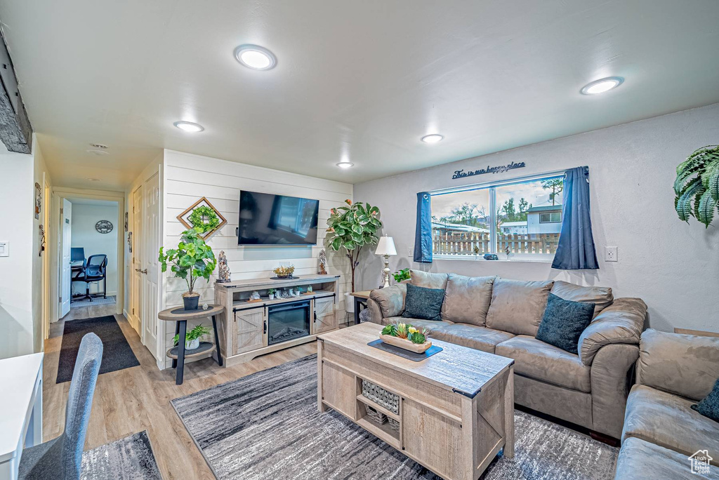 Living room with light wood-type flooring, a glass covered fireplace, and recessed lighting