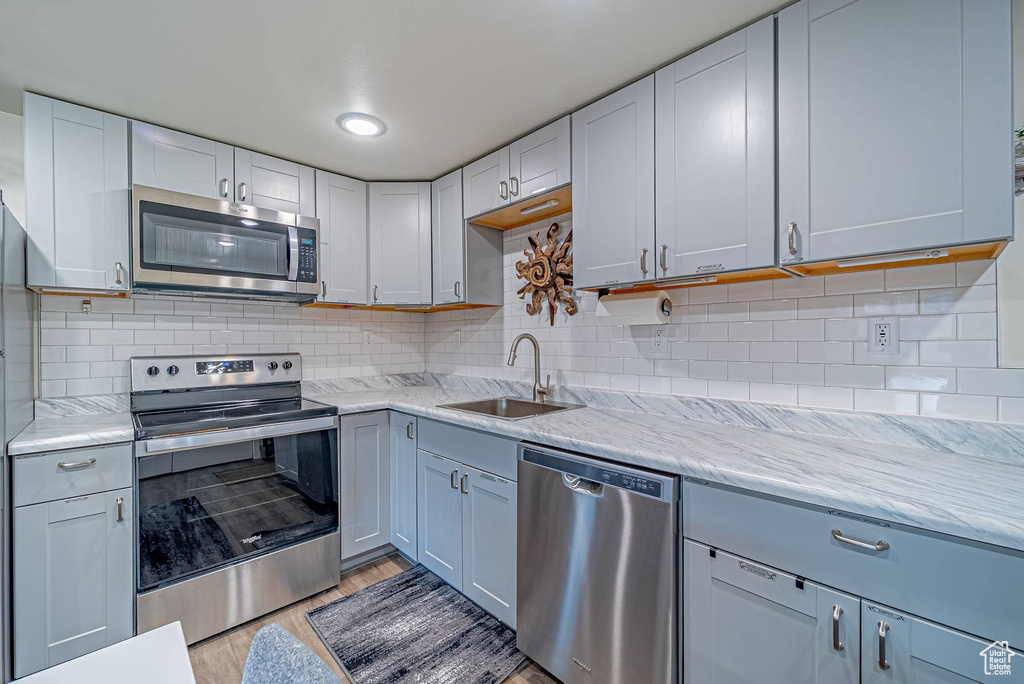 Kitchen featuring tasteful backsplash, a sink, light wood-style floors, light stone countertops, and stainless steel appliances