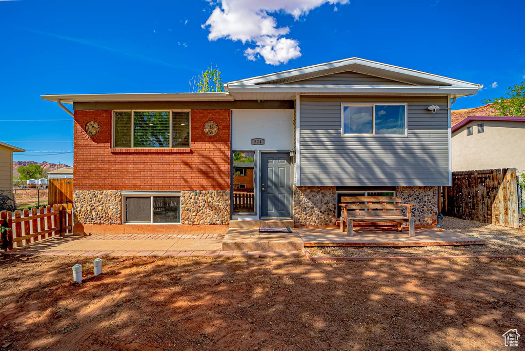 Raised ranch with fence, stone siding, and a patio