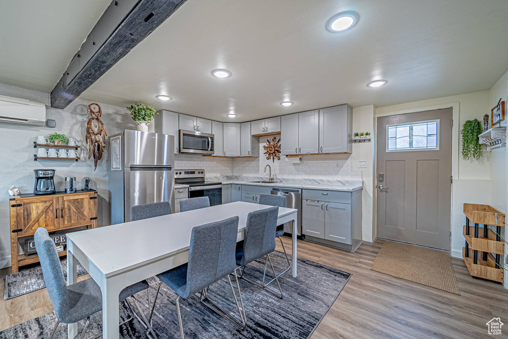Kitchen with a wall mounted AC, appliances with stainless steel finishes, light wood-type flooring, decorative backsplash, and a sink