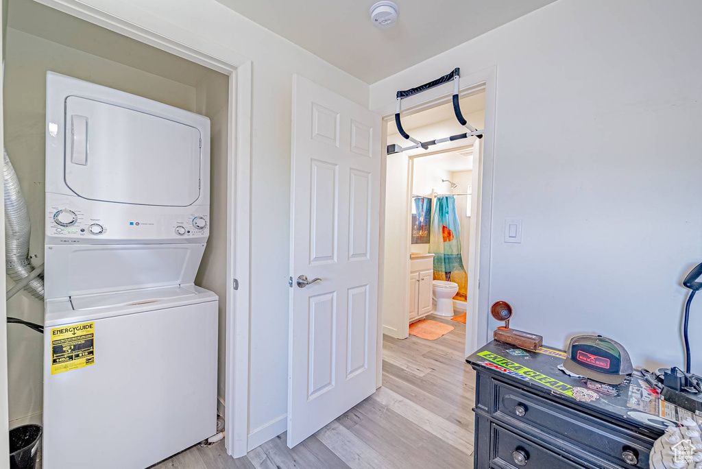 Washroom featuring baseboards, light wood-style floors, stacked washer / drying machine, and laundry area