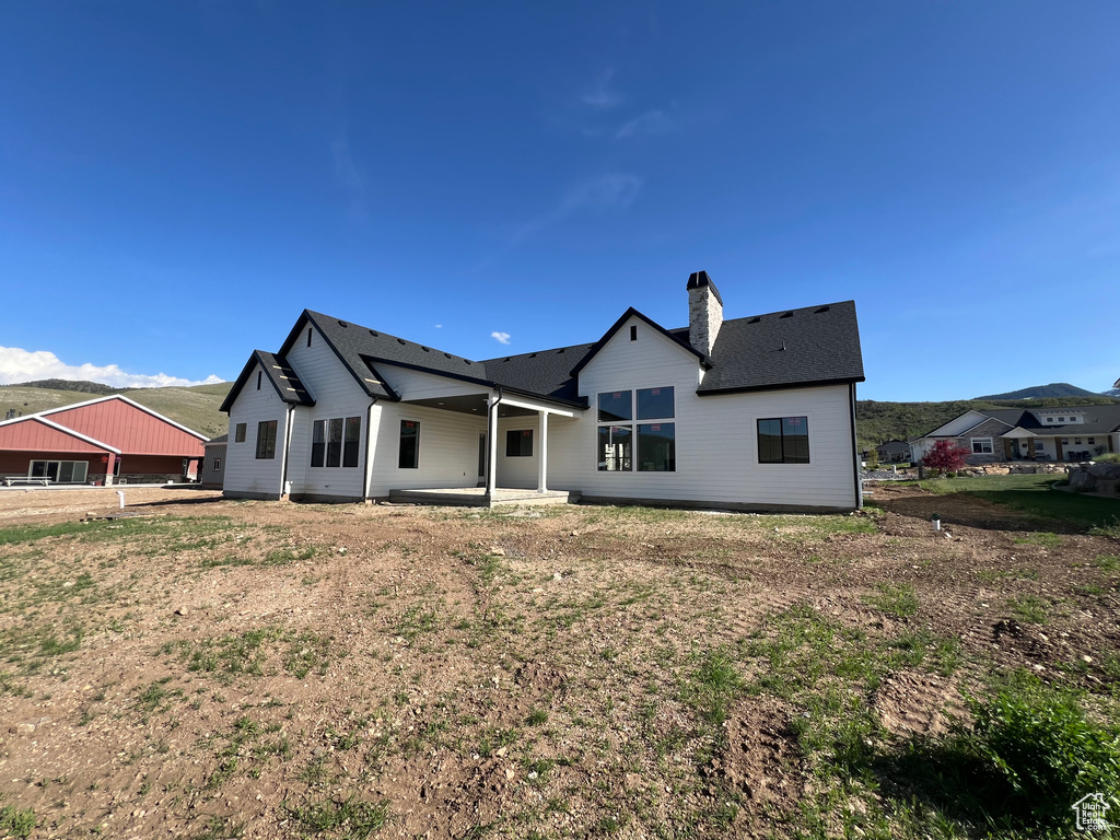 Back of property featuring a chimney, a patio, a mountain view, and roof with shingles