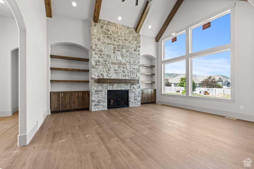 Unfurnished living room with beamed ceiling, high vaulted ceiling, light wood-type flooring, arched walkways, and a fireplace
