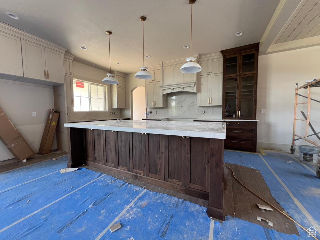 Kitchen featuring decorative backsplash, a spacious island, pendant lighting, baseboards, and light stone counters
