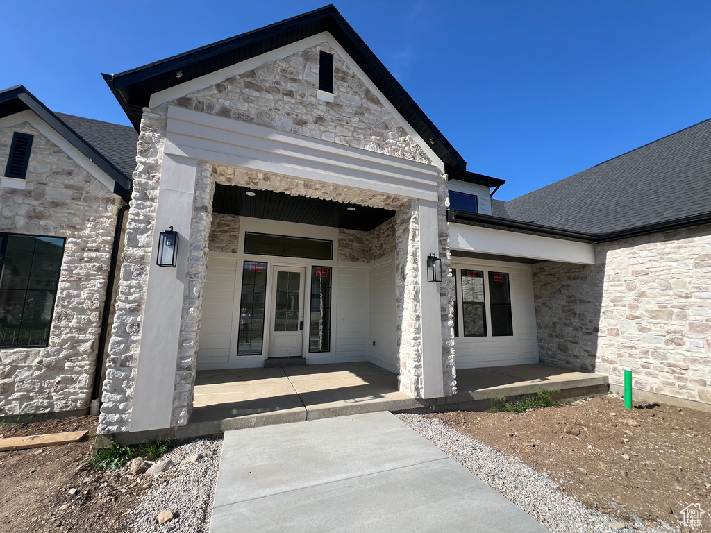 Entrance to property featuring stone siding, a porch, and a shingled roof