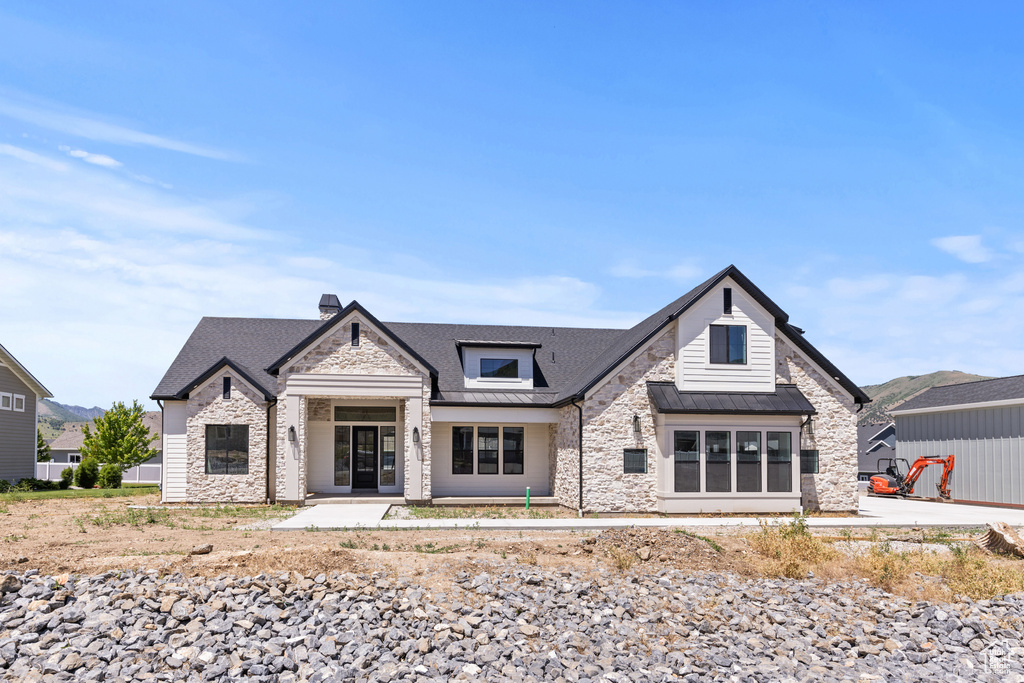 View of front of home with stone siding, a standing seam roof, a metal roof, a chimney, and a patio area