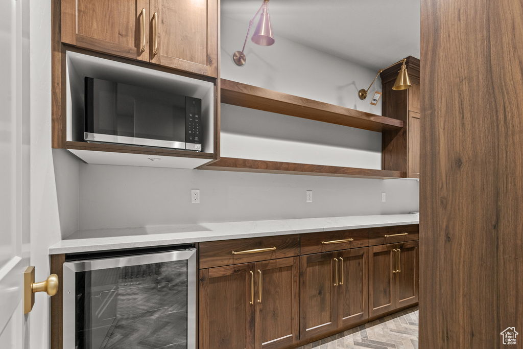 Kitchen featuring beverage cooler, stainless steel microwave, open shelves, and light countertops