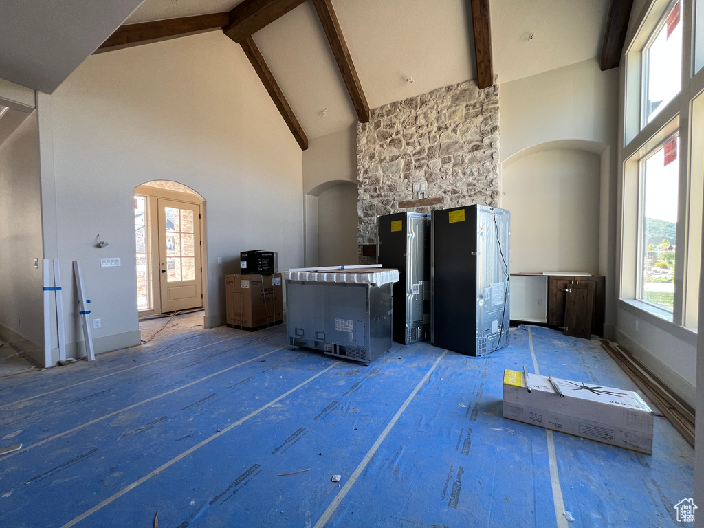 Unfurnished living room featuring high vaulted ceiling, arched walkways, and beamed ceiling