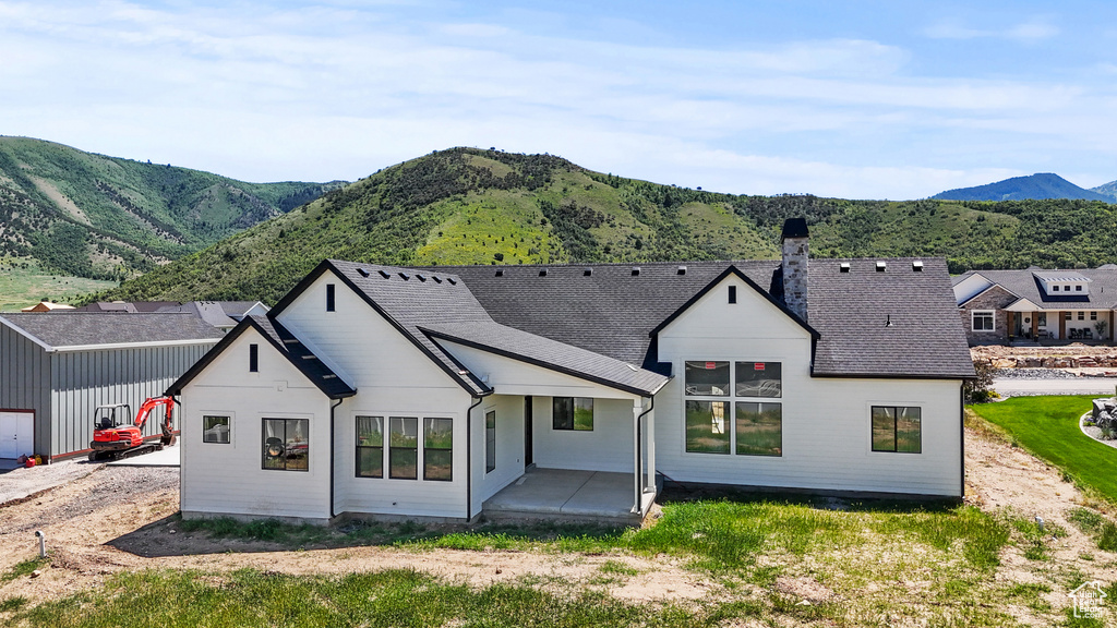 Rear view of property featuring a mountain view, a chimney, a patio area, and roof with shingles