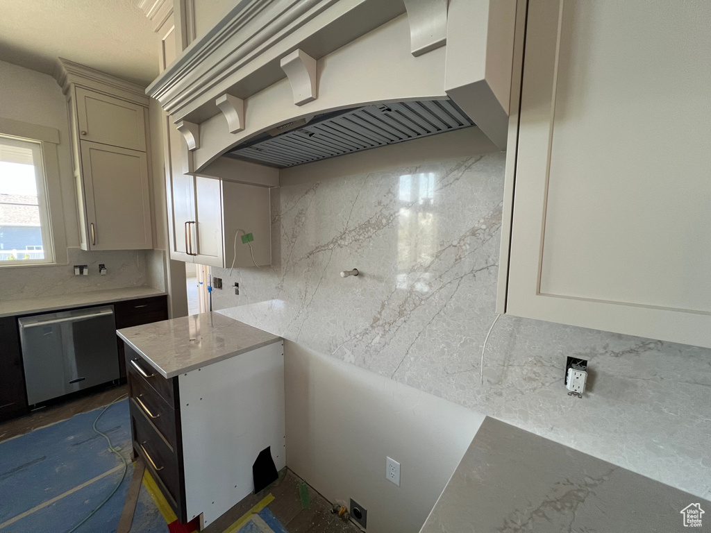Kitchen with stainless steel dishwasher, custom exhaust hood, backsplash, and light stone countertops