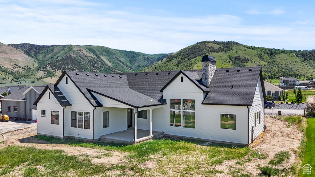 Rear view of house featuring a chimney, a mountain view, roof with shingles, and a patio area