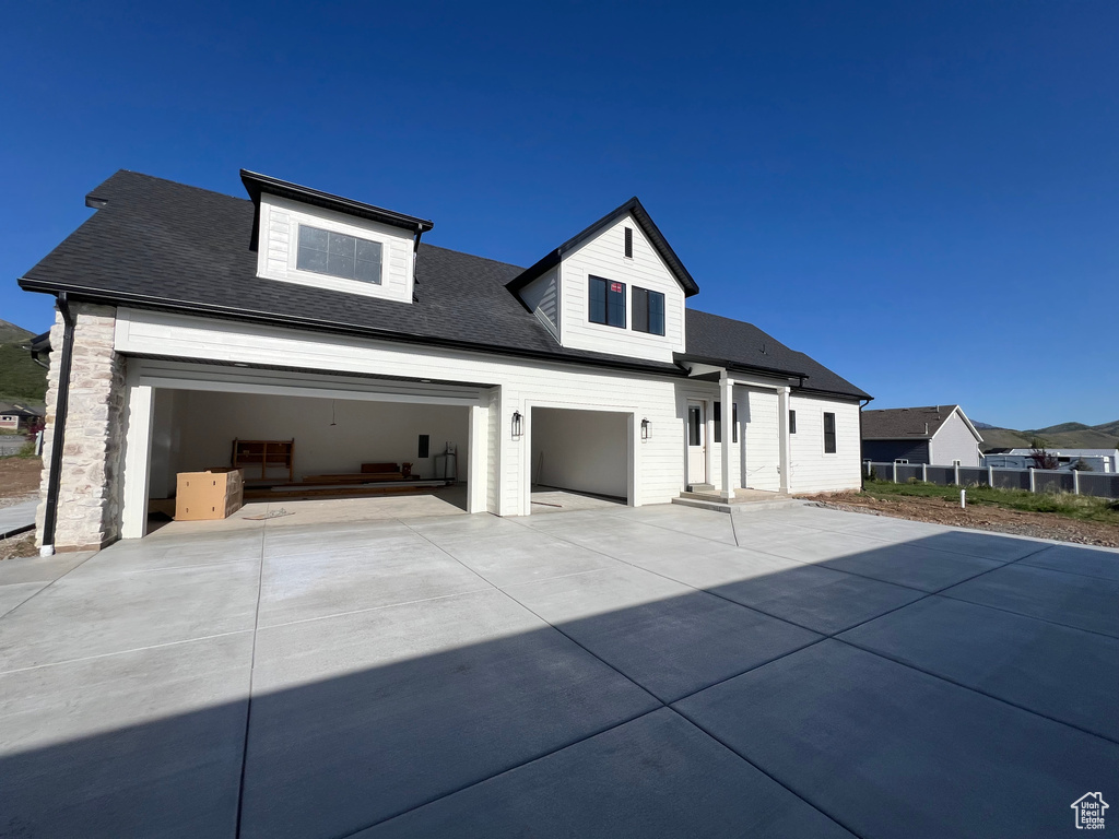 View of front of property featuring driveway, roof with shingles, and fence