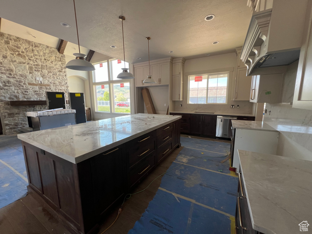 Kitchen featuring dishwasher, light stone counters, a center island, pendant lighting, and a textured ceiling