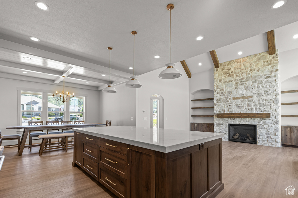 Kitchen with beamed ceiling, light wood-style floors, a kitchen island, a fireplace, and a chandelier