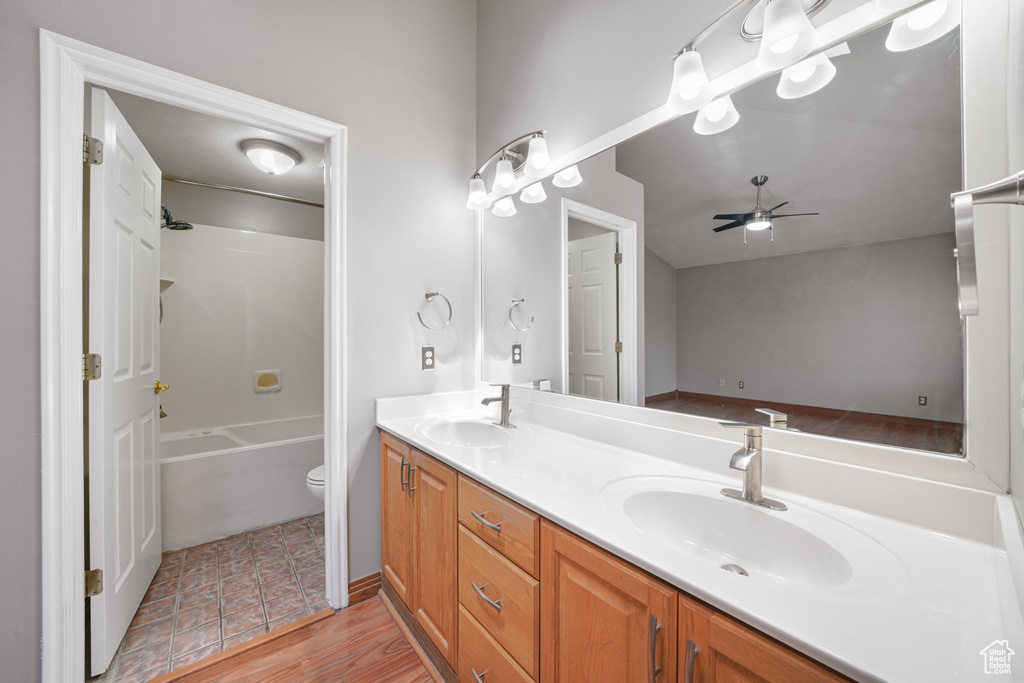 Full bath with toilet, double vanity, a sink, and a ceiling fan