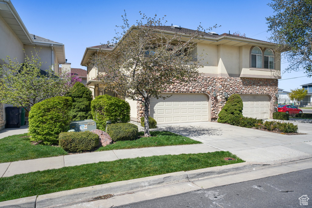 View of front of house with a garage, stucco siding, stone siding, and concrete driveway