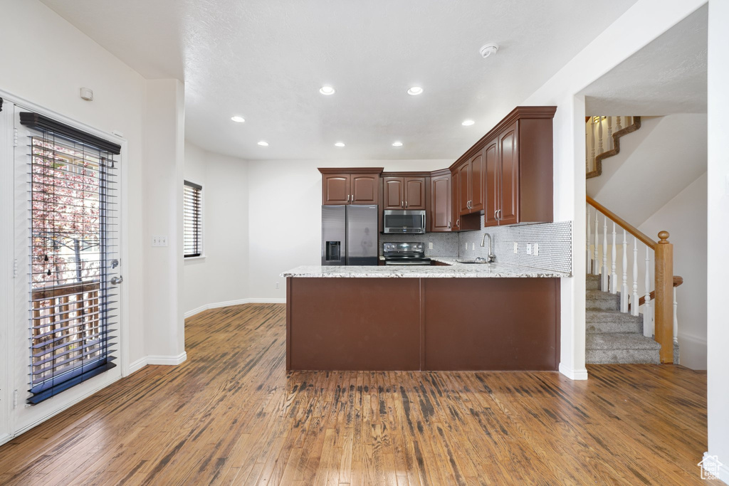Kitchen with tasteful backsplash, a peninsula, recessed lighting, appliances with stainless steel finishes, and wood-type flooring