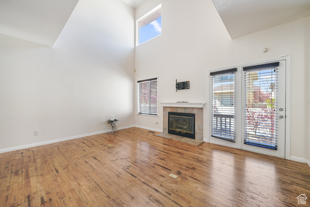 Unfurnished living room with wood finished floors, high vaulted ceiling, baseboards, and a tile fireplace
