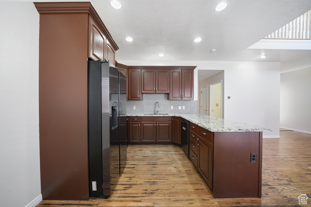 Kitchen featuring stainless steel fridge with ice dispenser, baseboards, a peninsula, light wood-style floors, and a sink