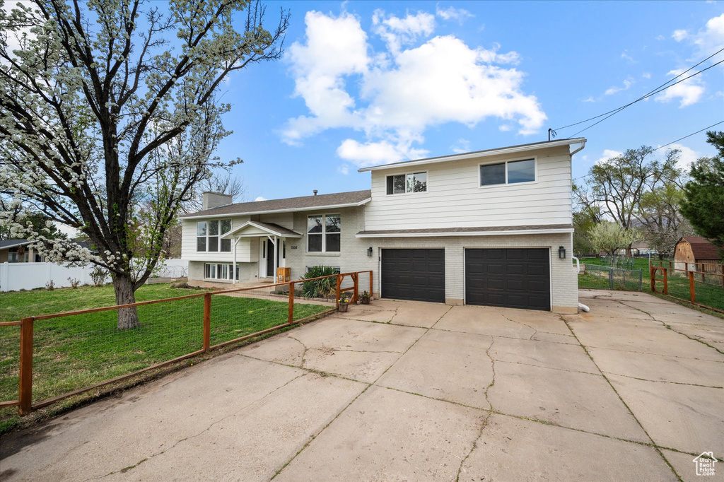 Split level home featuring an attached garage, a fenced front yard, brick siding, a front lawn, and driveway