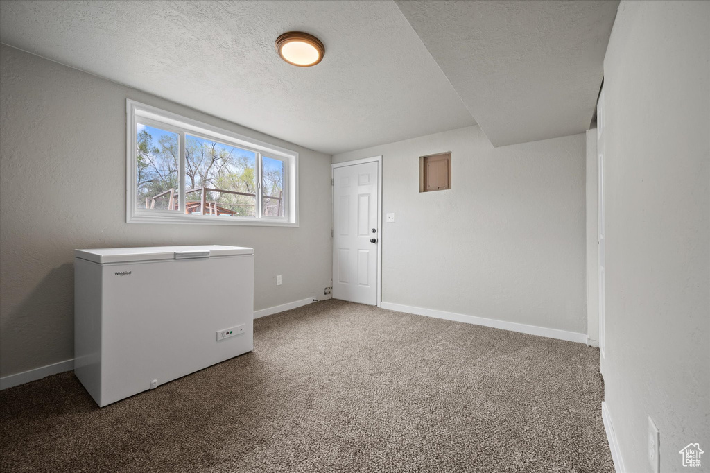 Carpeted spare room featuring a textured ceiling and baseboards