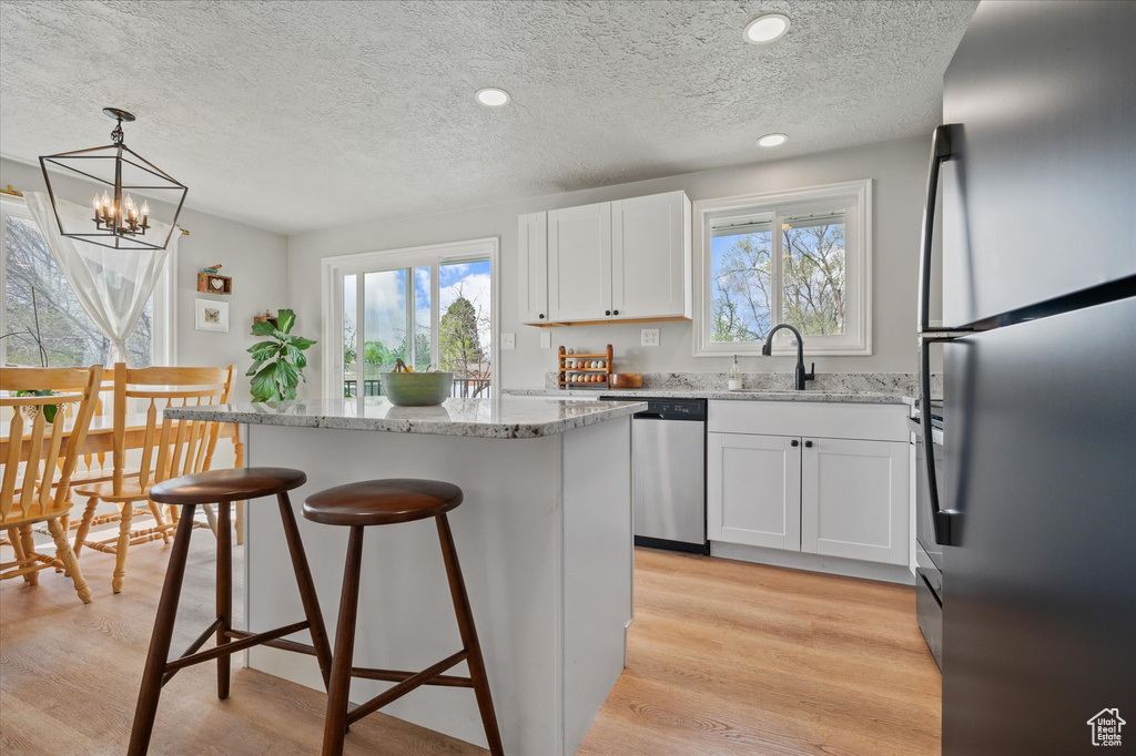 Kitchen featuring a center island, a textured ceiling, light stone countertops, a kitchen bar, and stainless steel appliances