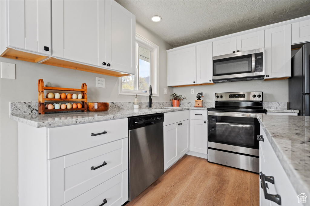 Kitchen featuring white cabinets, a sink, light wood-type flooring, appliances with stainless steel finishes, and light stone counters