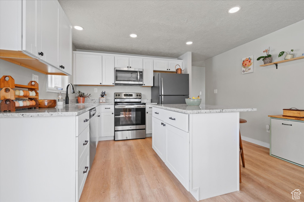 Kitchen featuring a center island, a textured ceiling, white cabinets, stainless steel appliances, and light wood finished floors