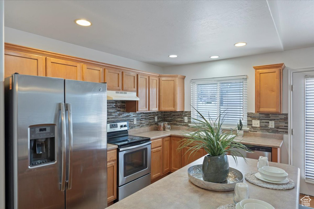 Kitchen with light countertops, appliances with stainless steel finishes, under cabinet range hood, recessed lighting, and backsplash