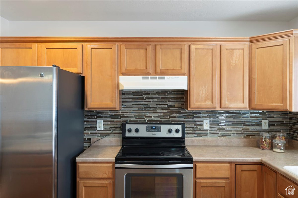 Kitchen featuring under cabinet range hood, tasteful backsplash, light countertops, and appliances with stainless steel finishes