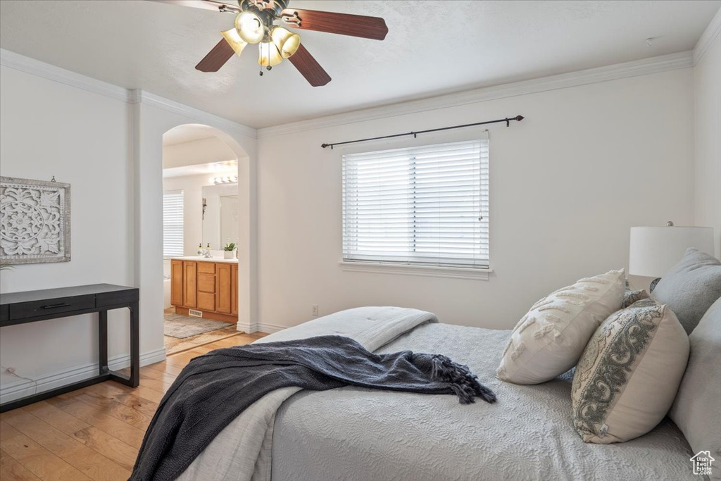 Bedroom with baseboards, arched walkways, ornamental molding, light wood-type flooring, and a ceiling fan